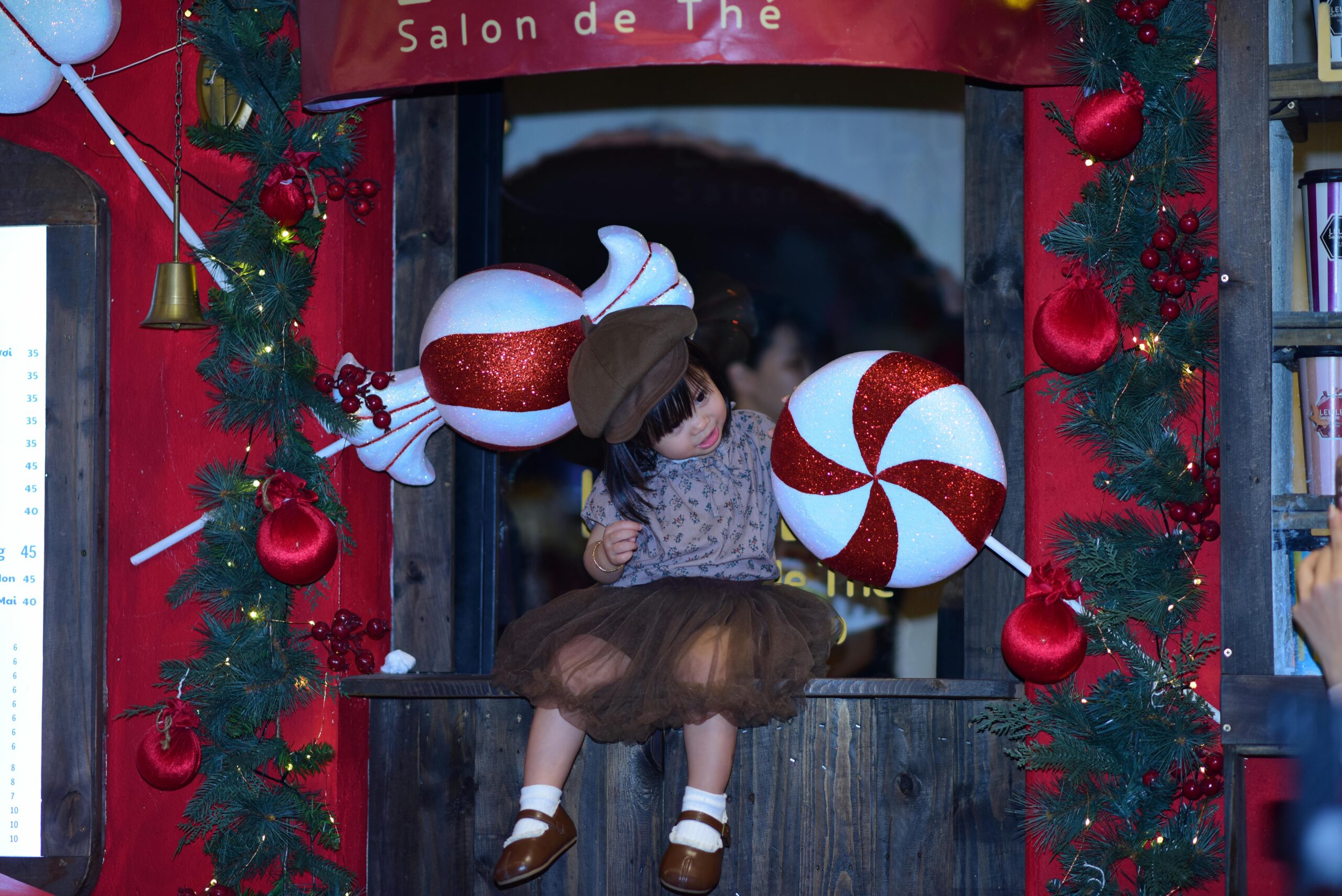 A child sits in a window adorned with Christmas-themed decorations.