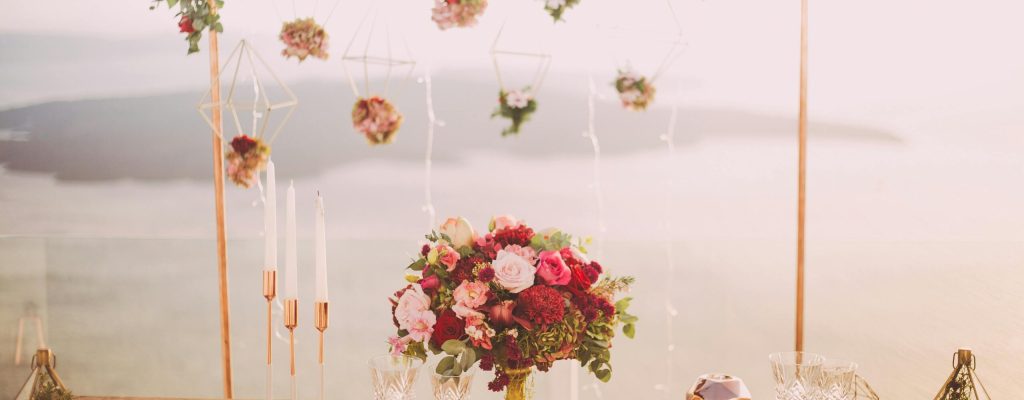 Romantic dining setup with flowers and candles overlooking Santorini waterscape at sunset.