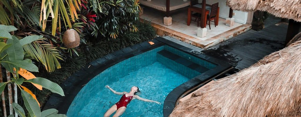 A woman enjoying leisure time floating in a tropical resort pool surrounded by lush greenery.